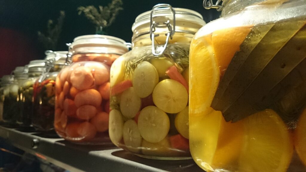 Several jars of brined carrots, beans and cucumbers lined up on a wooden shelf