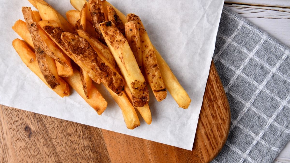 A close-up shot of crispy, golden-brown chicken wings perfectly cooked in an air fryer basket, with a hand reaching in to rem...