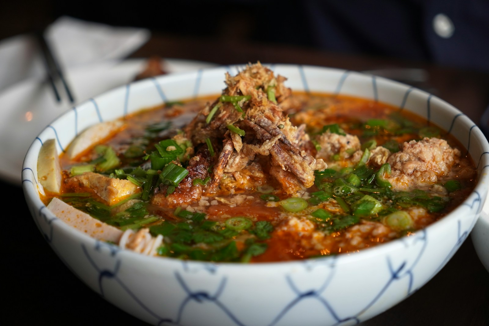 Grilled pork patties and pork belly in a ceramic bowl of amber nuoc cham with julienned vegetables, served with rice vermicelli and fresh herbs