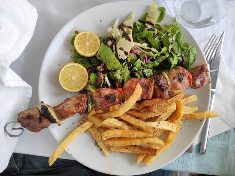 Grilled chicken souvlaki skewers on a wooden board with warm pita bread, creamy tzatziki sauce, sliced tomatoes, and red onion
