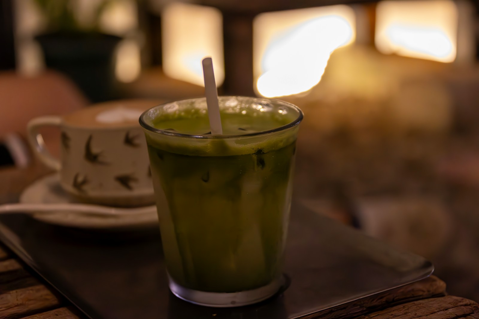 Iced hojicha latte in a tall glass with vanilla cold foam cap and hojicha dust on top, cinnamon stick on wooden counter