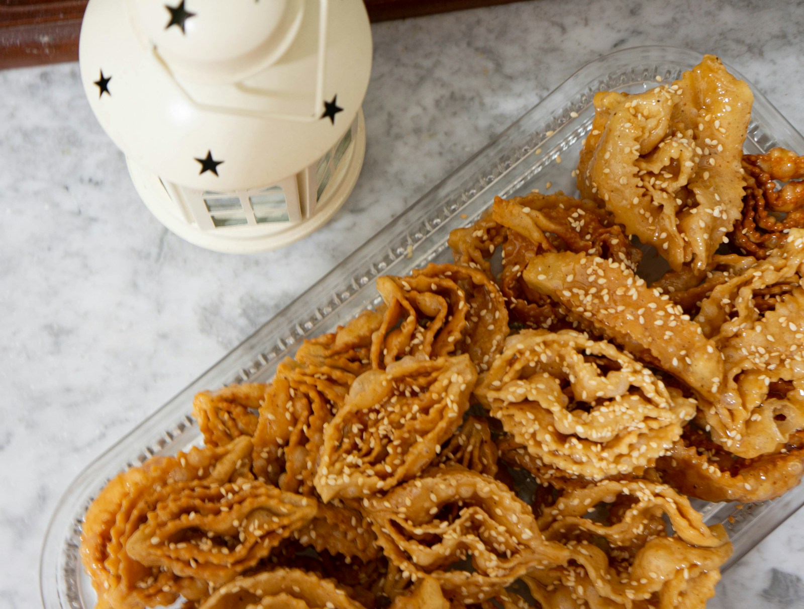 Slice of golden knafeh topped with crushed pistachios on a ceramic plate with orange blossom syrup