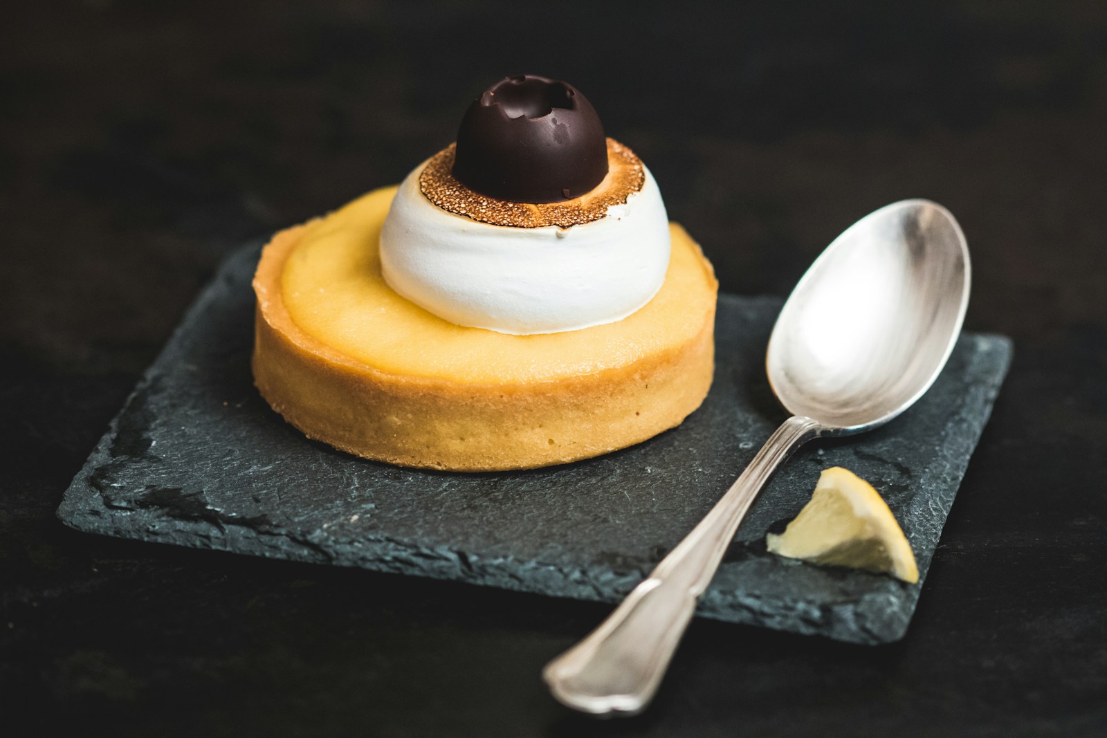 Slice of lemon tart with cream and spoon on rustic surface