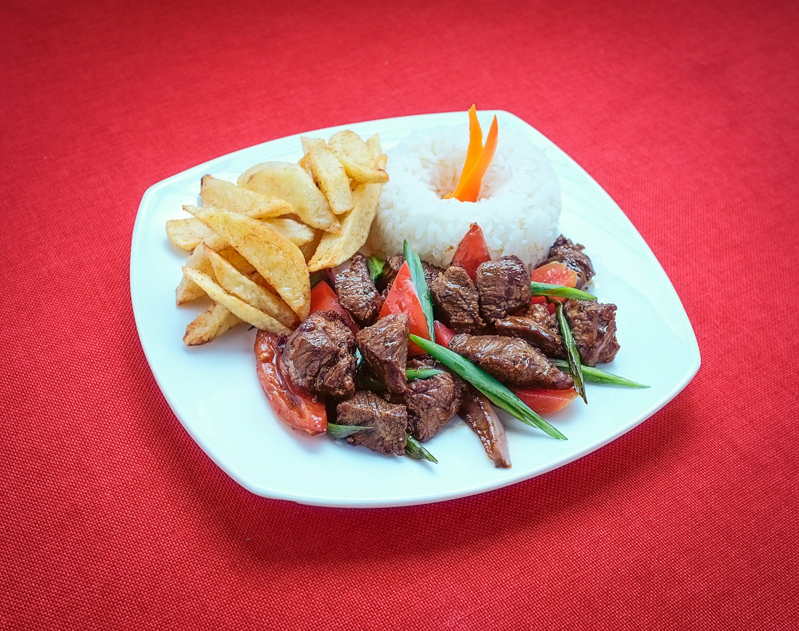 Wok of lomo saltado with seared beef strips, red onion wedges, tomato, and golden fries in a glossy brown sauce