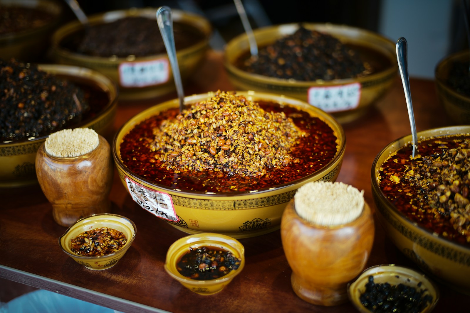 Bowls of Sichuan chili paste, fermented black beans, and dried peppercorns on a wooden surface