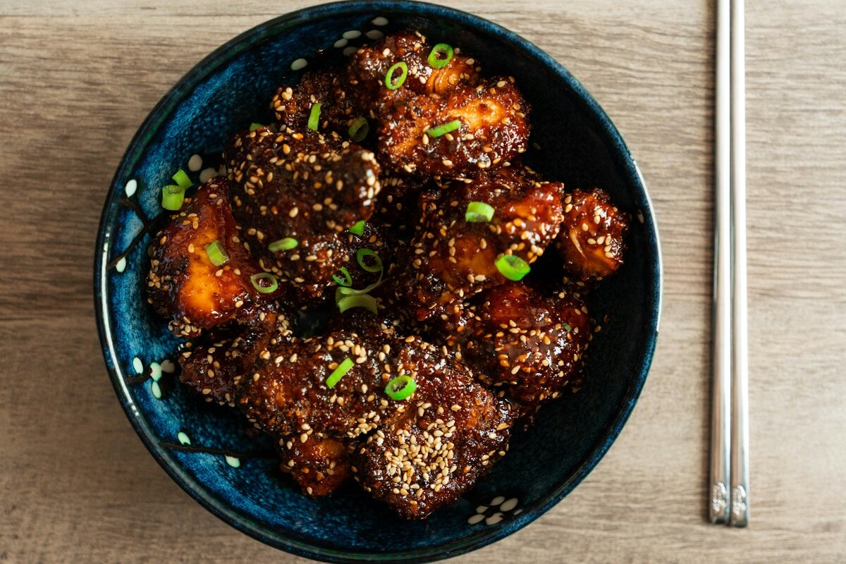 A platter of double-fried Korean chicken wings glazed in glossy red gochujang sauce with sesame seeds and green onion