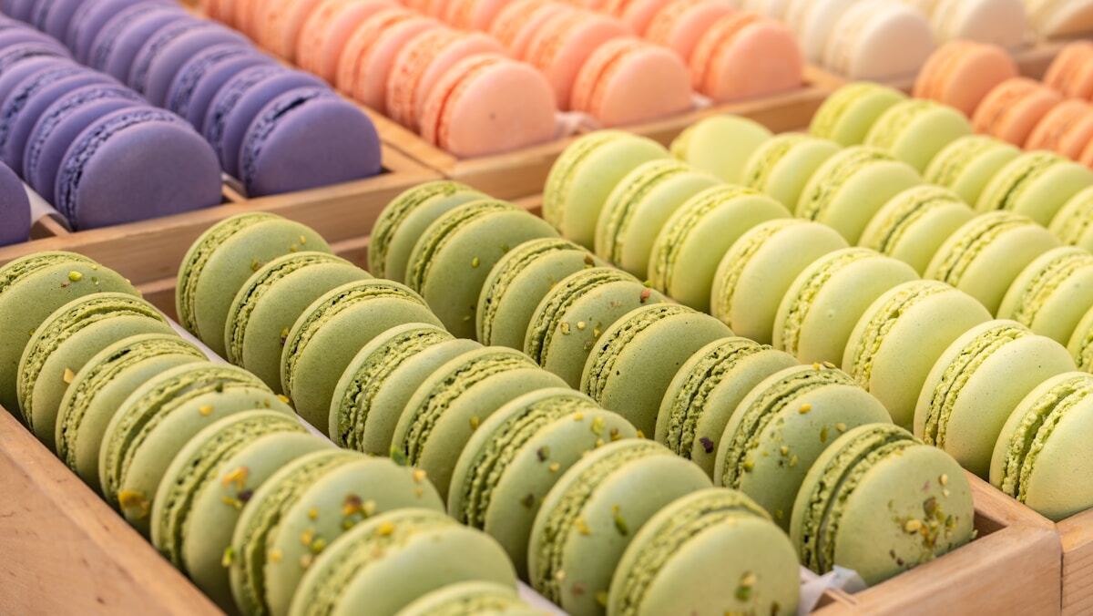 A tray of pastel-colored French macarons - pistachio green and rose pink - with smooth domes and ruffled feet, sandwiched with buttercream