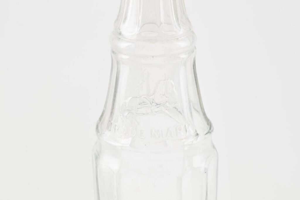 A bottle of dark fruit vinegar syrup next to a glass of sparkling water