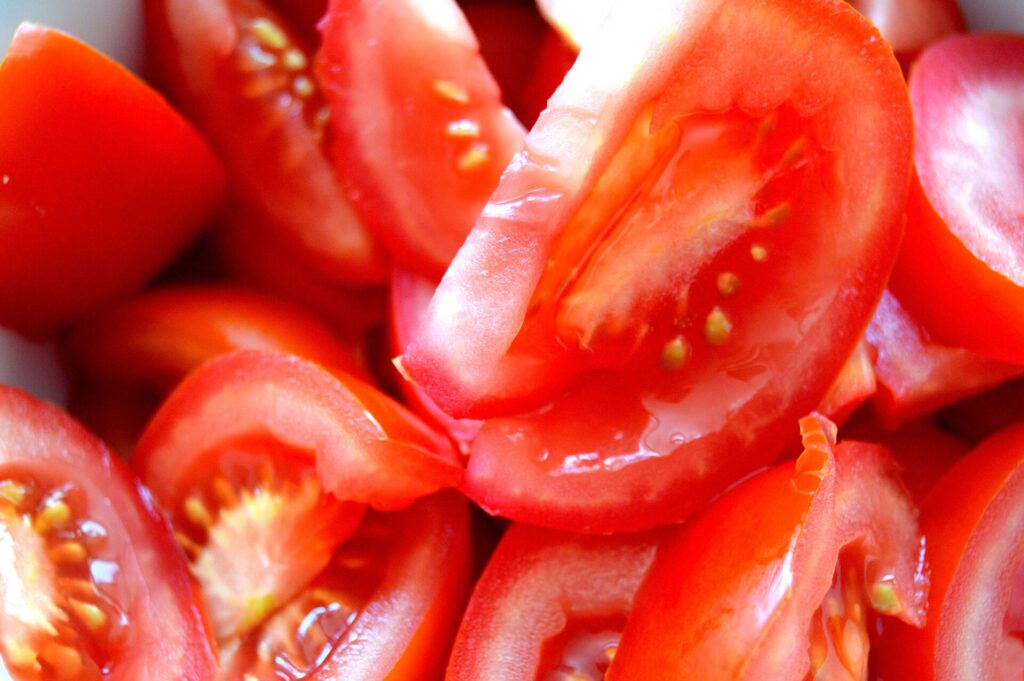 Thick tomato slices resting on a wooden board beside a small dish of salt