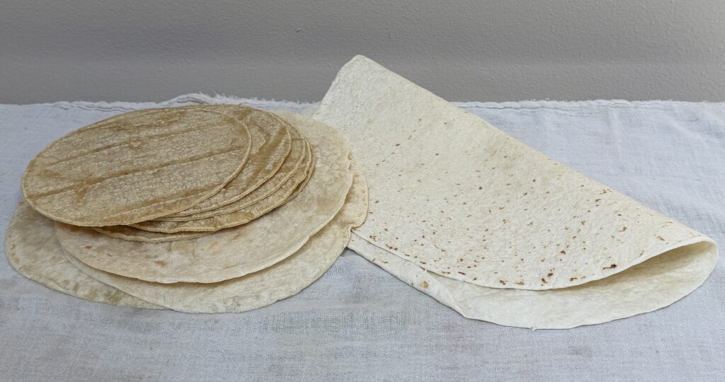 A stack of warm handmade corn tortillas wrapped in a folded cotton cloth