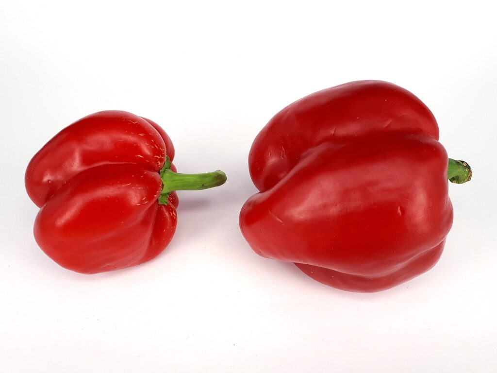 Whole red and green bell peppers arranged on a wooden kitchen table