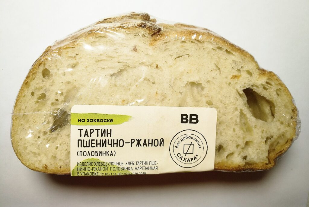 A dark rye loaf partly sliced on a board showing its tight, even crumb