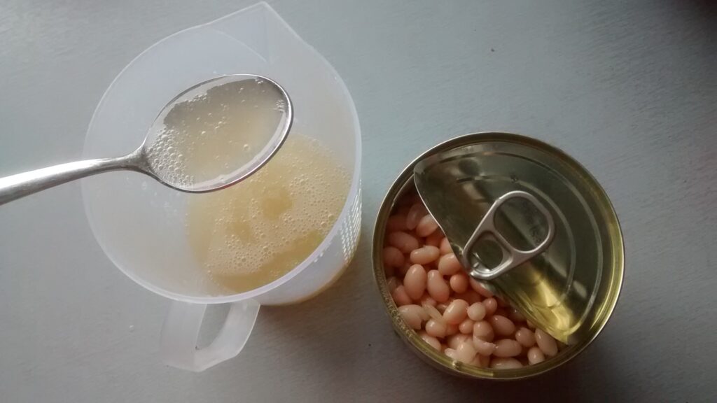 Cooked white beans in a shallow earthenware pot with a wooden spoon resting in them