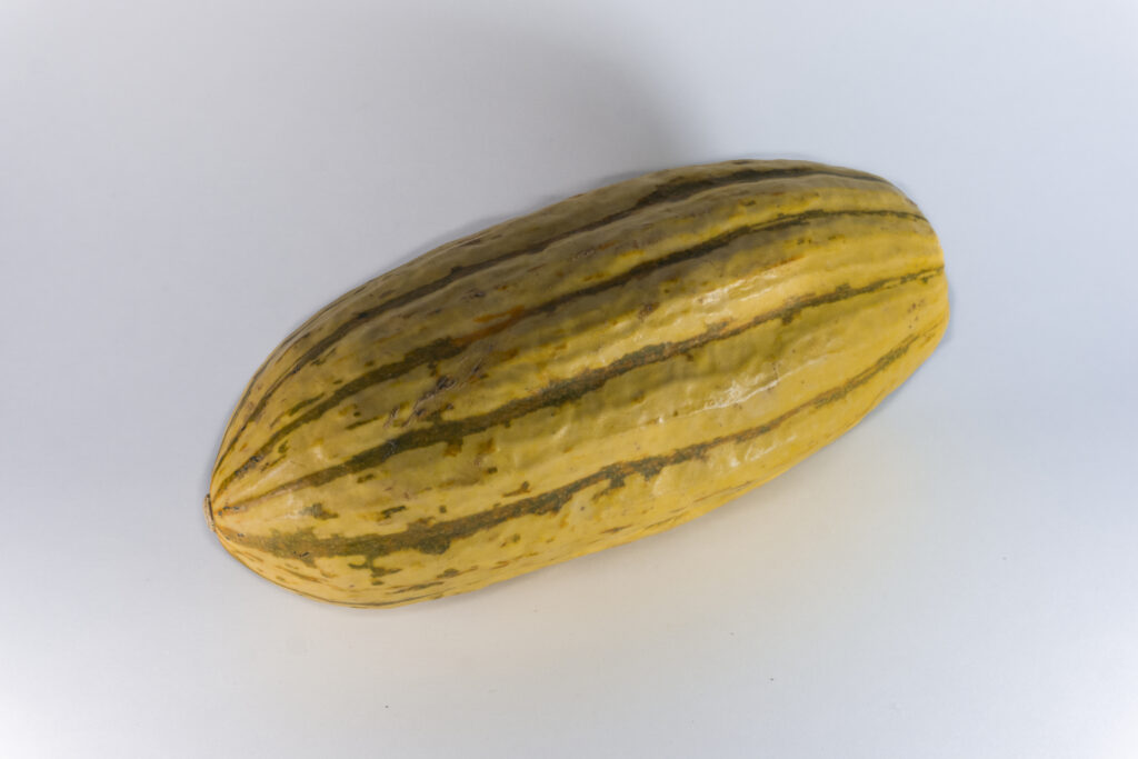 Striped delicata and dark acorn squash piled together in a shallow wooden bin