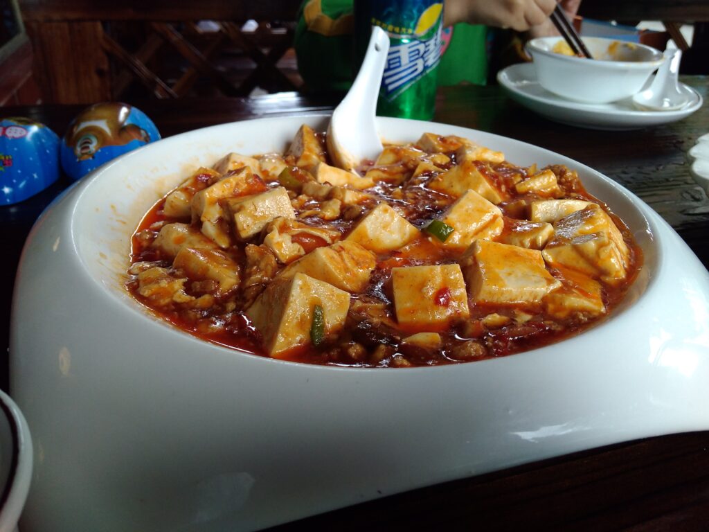 A bowl of braised tofu in red sauce dusted with ground pepper and scallion