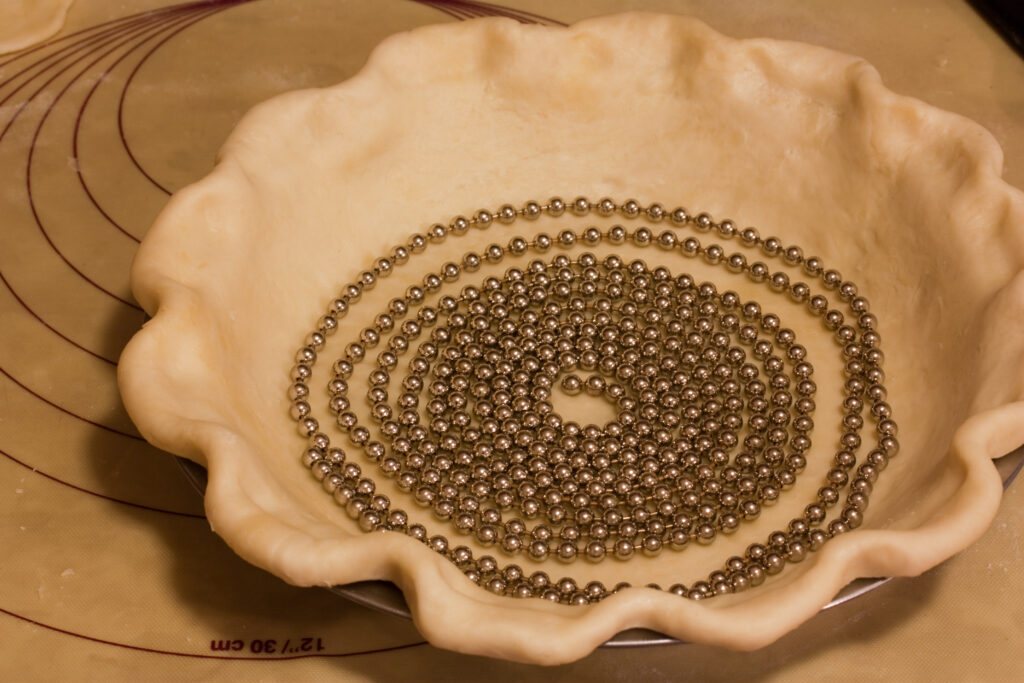 Dried beans filling a parchment lined pastry shell right up to the rim