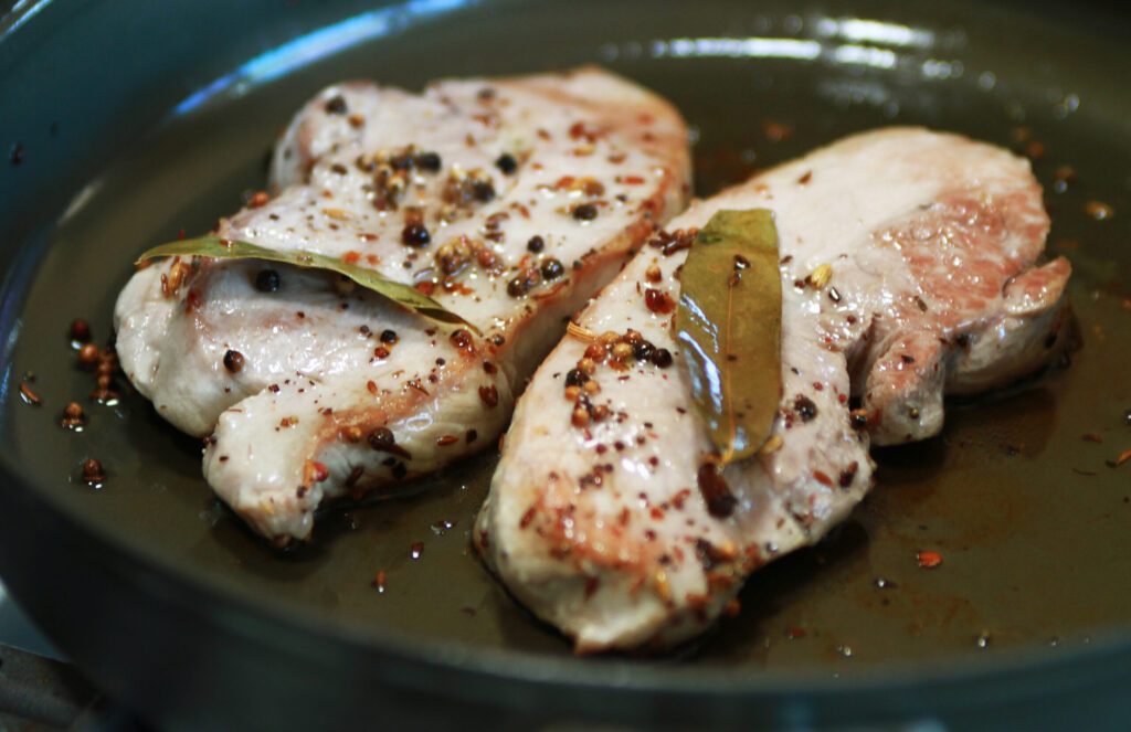 A browned pork chop searing in a cast iron skillet over high heat