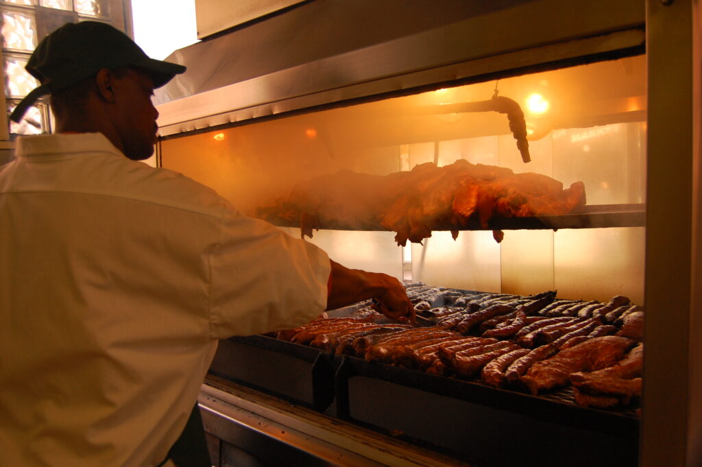 A drum smoker with the lid open showing meat on the cooking grate above coals