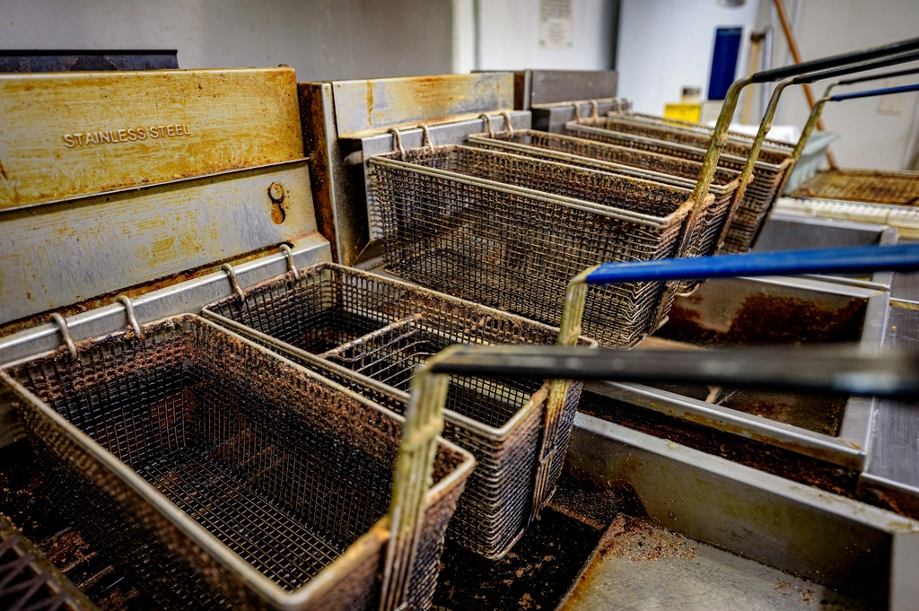 A wire basket lifted from a pot of hot frying oil with steam rising