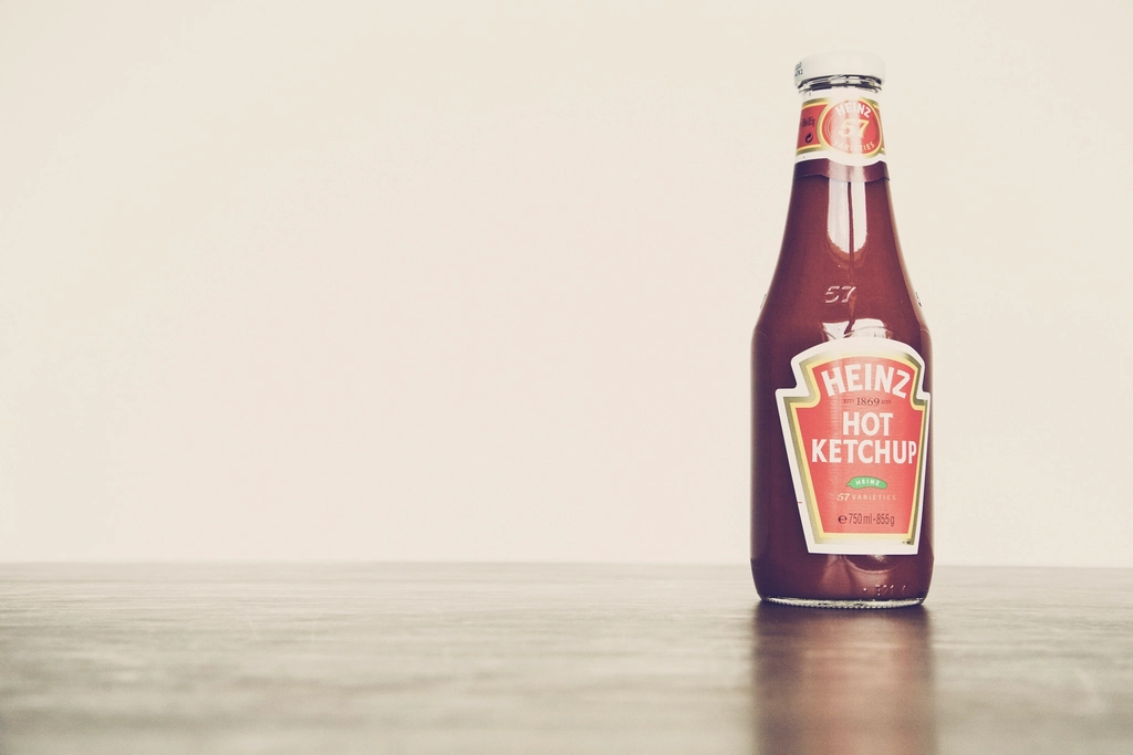 A small glass bottle of orange-red sauce beside a fine mesh sieve