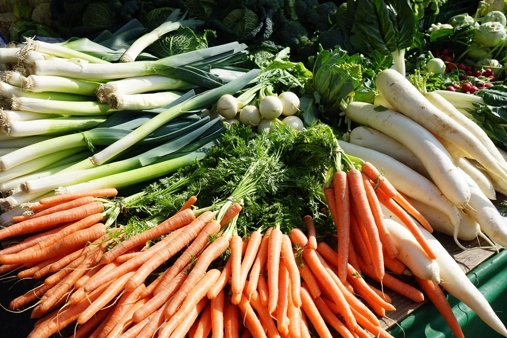 A leek, a carrot and a wedge of celeriac tied together on a market counter
