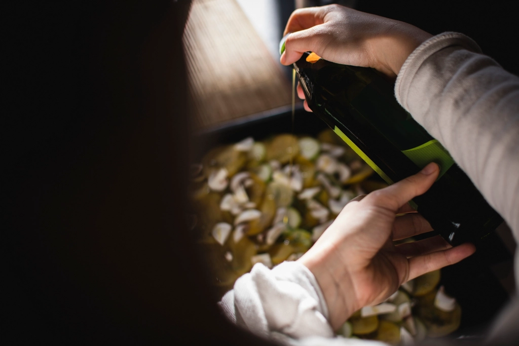 Green olive oil being poured from a bottle into a wide steel frying pan