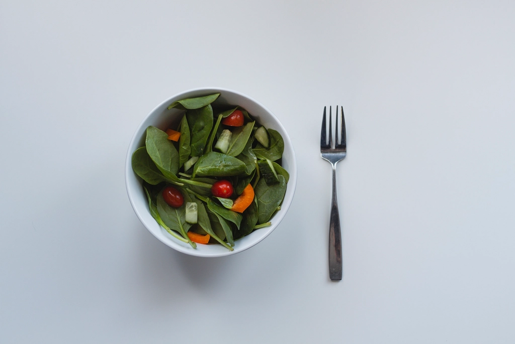 Dressed leaves in a wide wooden bowl with shallots and cracked pepper on top