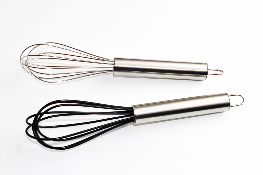 A metal whisk in a shallow bowl with oil being poured in a thin stream