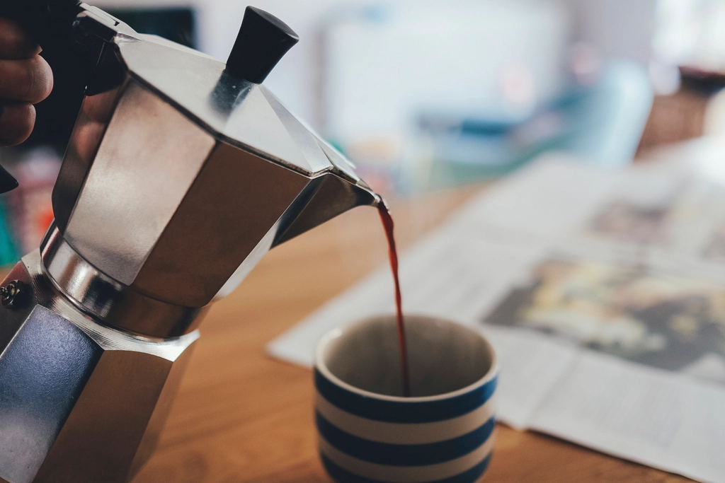 Boiling water poured from a kettle into a narrow steel flask on a worktop