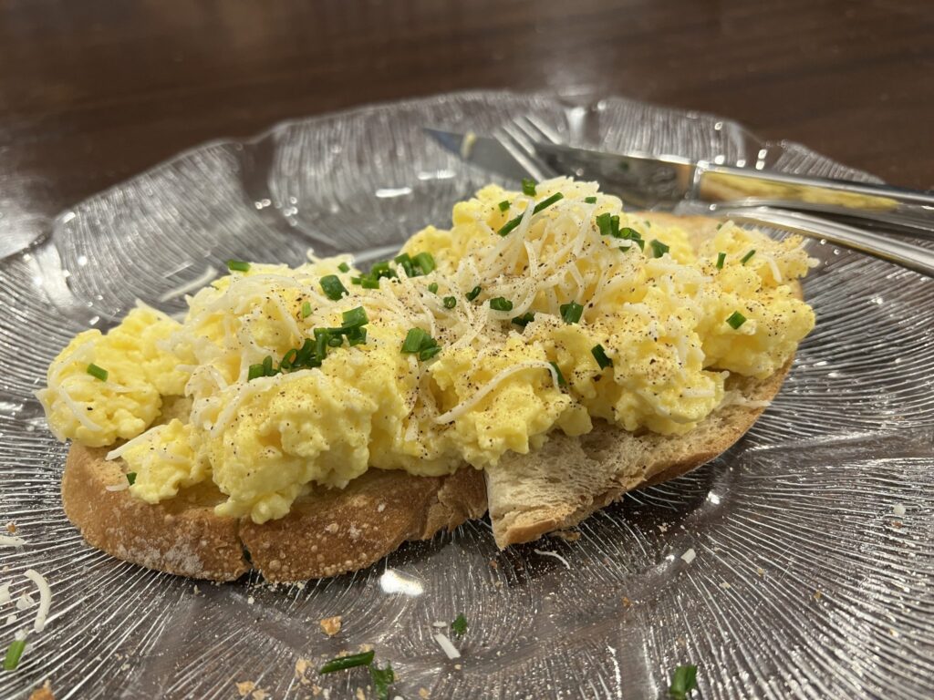 Loose scrambled eggs served beside buttered toast on a plain white plate