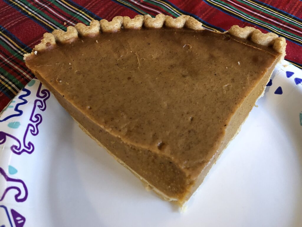 A wedge cut from a baked pumpkin pie showing a smooth set filling and a browned crust