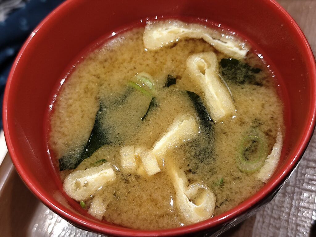A lacquer bowl of clear miso soup with cubes of tofu and sliced scallion