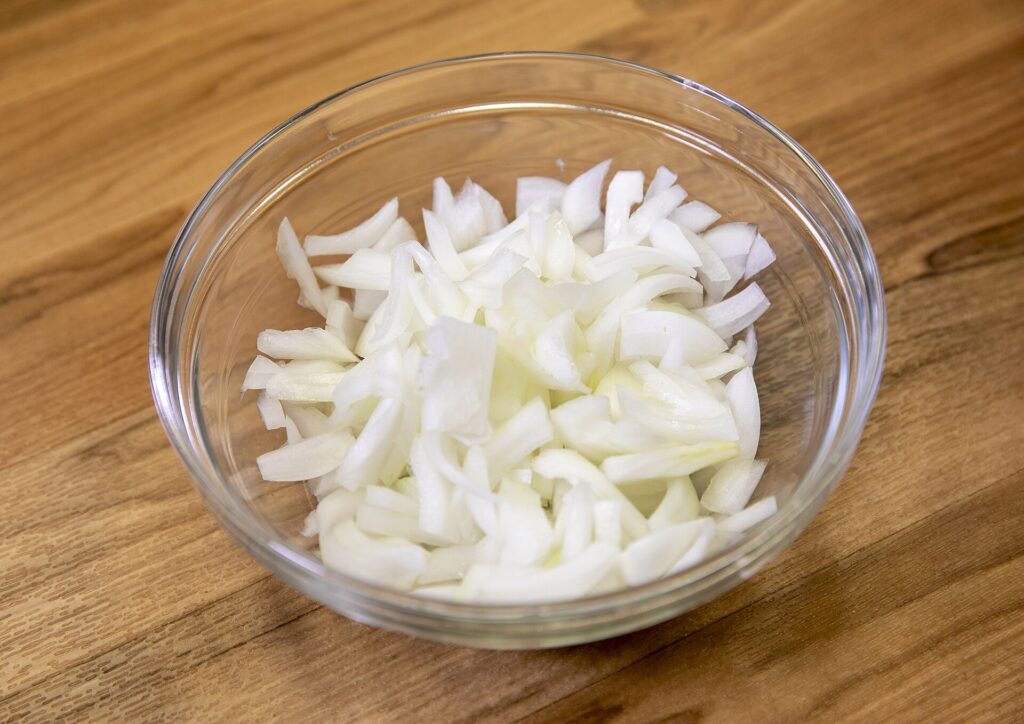 A bed of sliced onions softening in oil at the bottom of a heavy pot