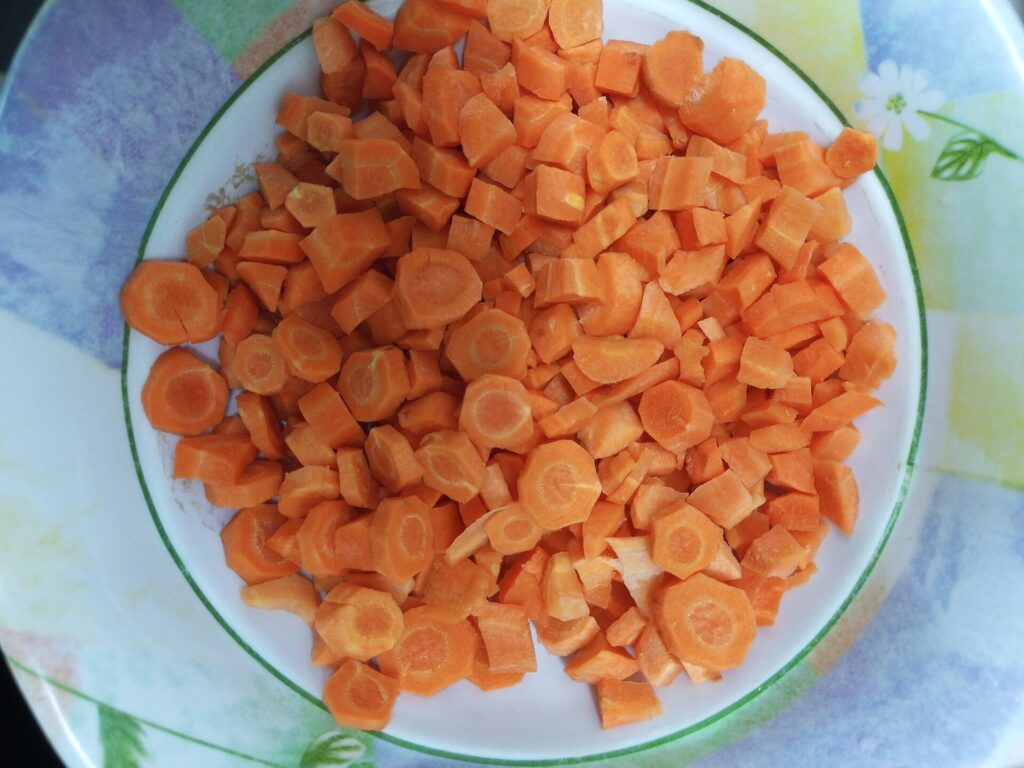 Peeled carrots cut into coins and batons on a wooden chopping board