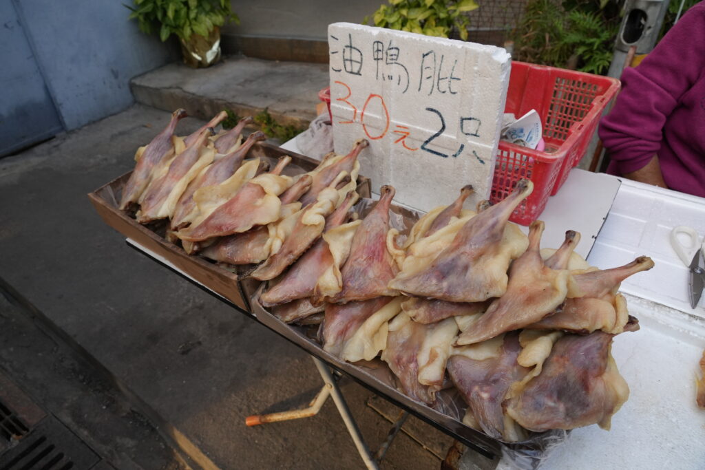 Four raw duck legs arranged skin side up on a tray with coarse salt and thyme