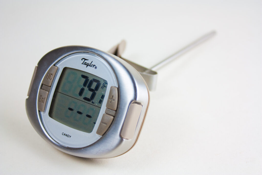A clip-on thermometer standing in a pan of boiling clear sugar syrup