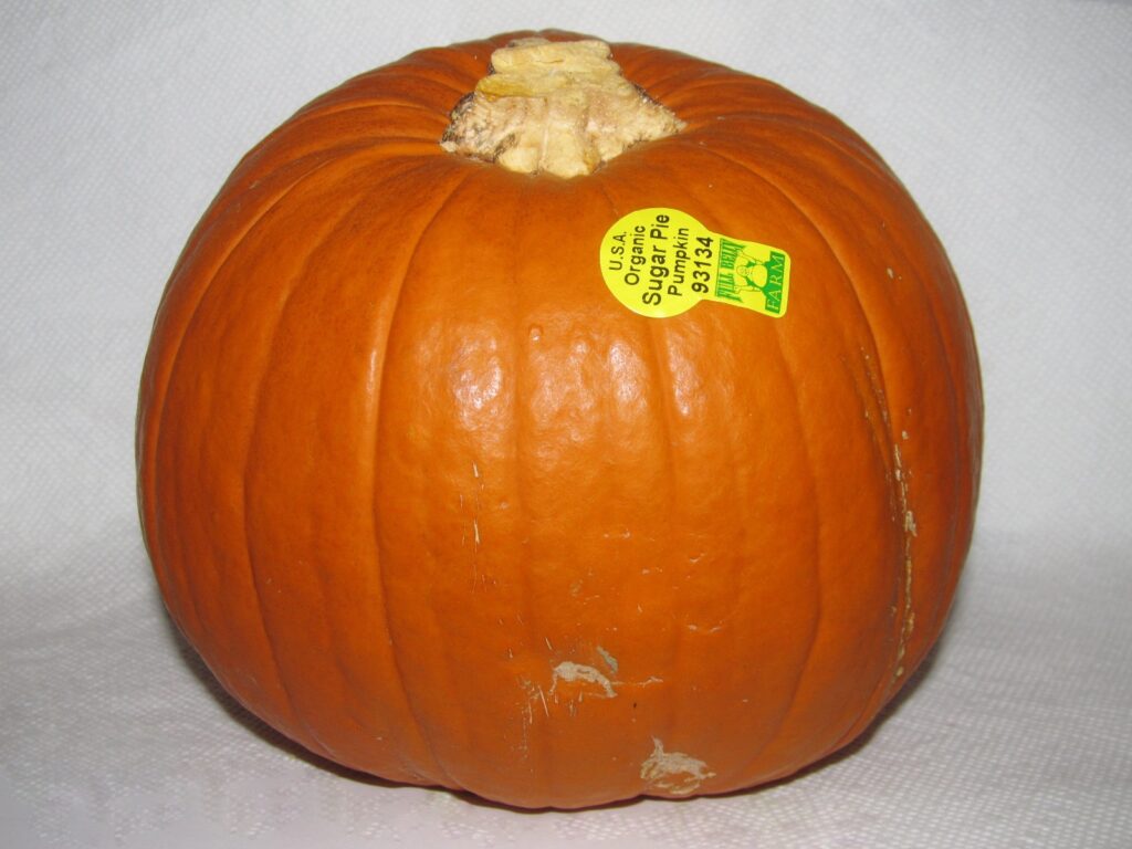 Several small deep orange pie pumpkins stacked in a wooden crate at a market