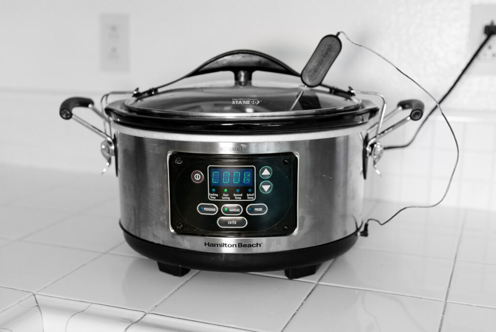Glazed cocktail meatballs simmering in sauce inside a small slow cooker