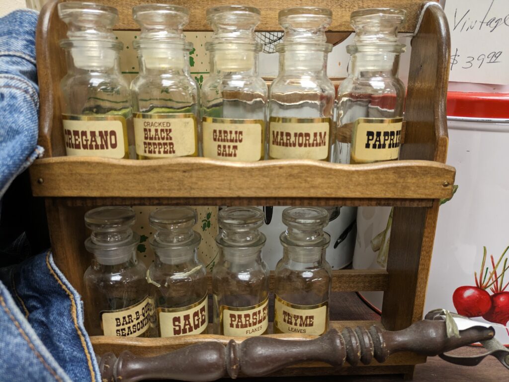 Glass jars of whole spices lined up on a wooden shelf away from the stove
