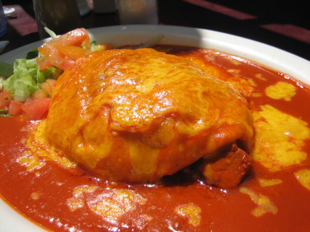 Blended dark red chile sauce being poured from a jug into a heavy pan