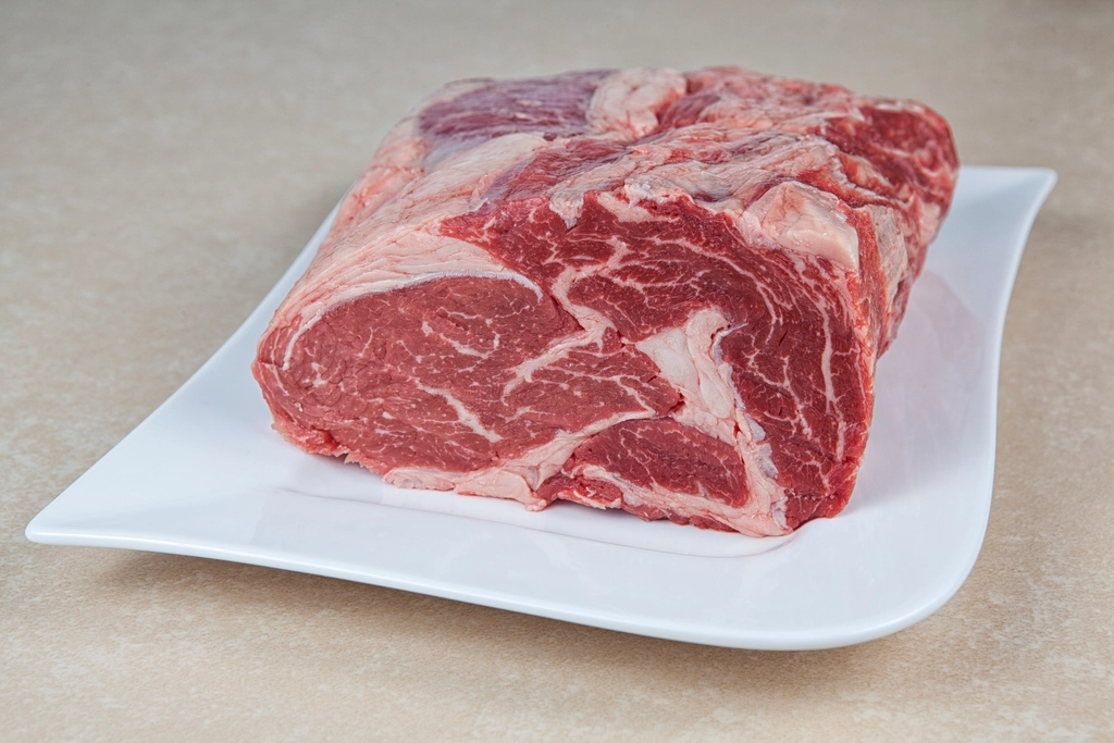 A whole raw beef shoulder roast on butcher paper showing fat seams and marbling