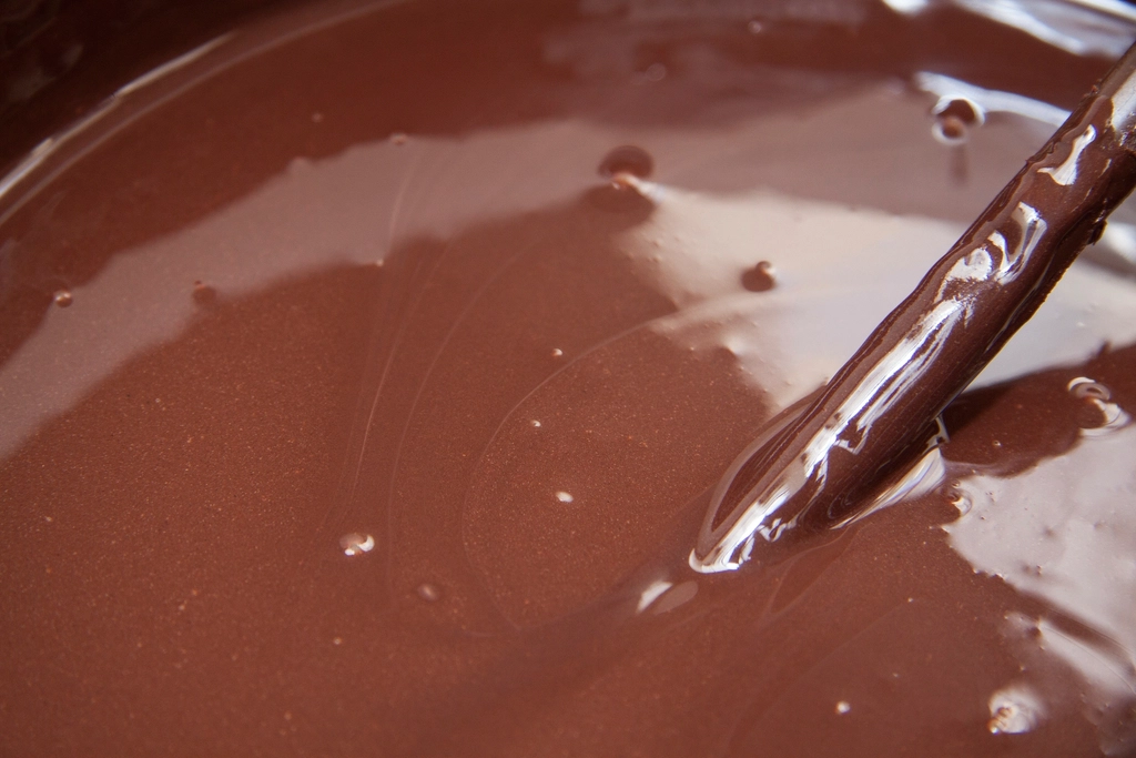 Smooth melted dark chocolate pooling in a glass bowl over a double boiler